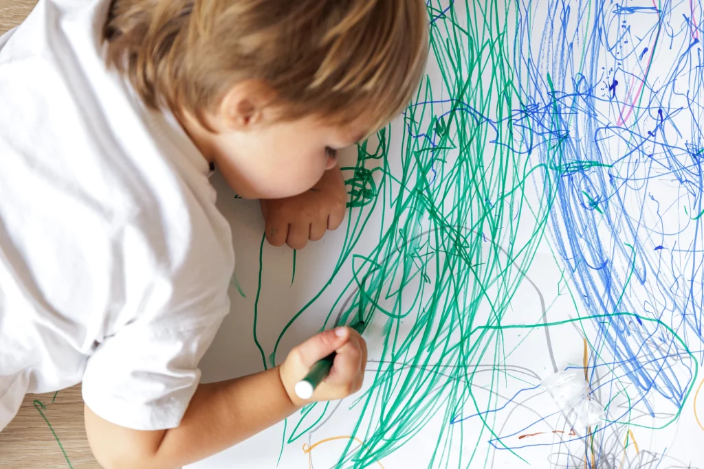 Un jeune enfant colorie sur une feuille de papier dans une micro-crèche.