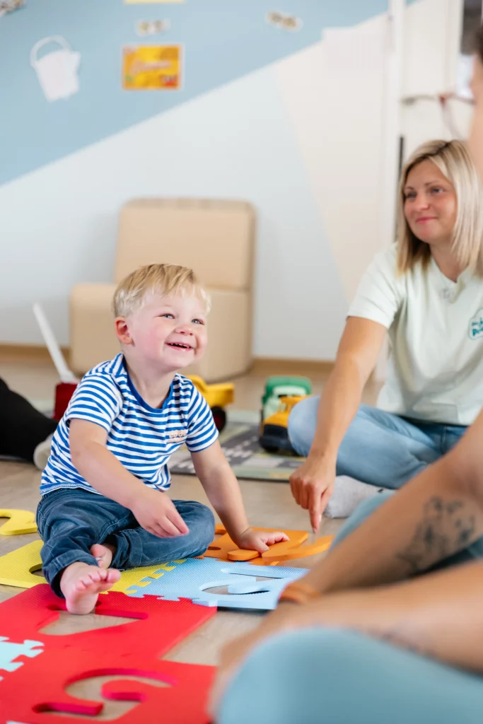 Des professionnelles partagent un moment de complicité avec un jeune enfant blond dans une micro-crèche.
