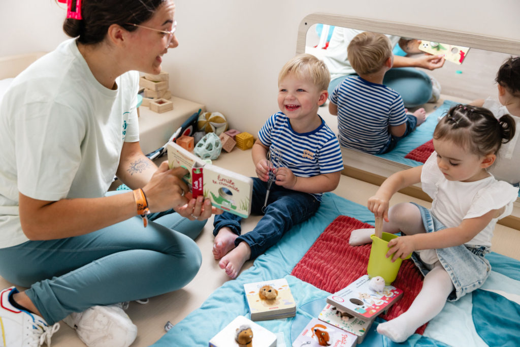 Professionnelle de la petite enfance lit un livre à deux enfants souriants
