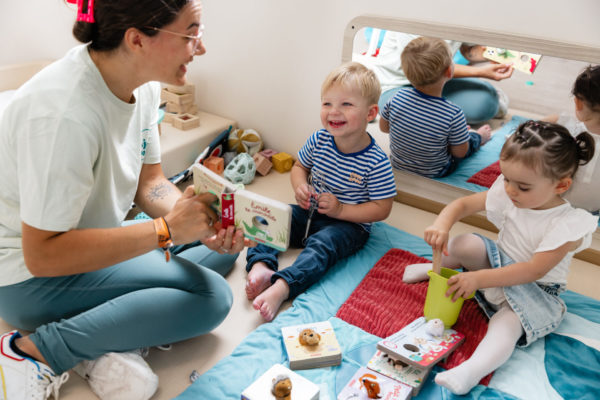 Professionnelle de la petite enfance lit un livre à deux enfants souriants