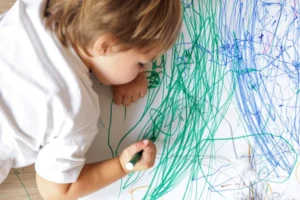 Un jeune enfant colorie sur une feuille de papier dans une micro-crèche.